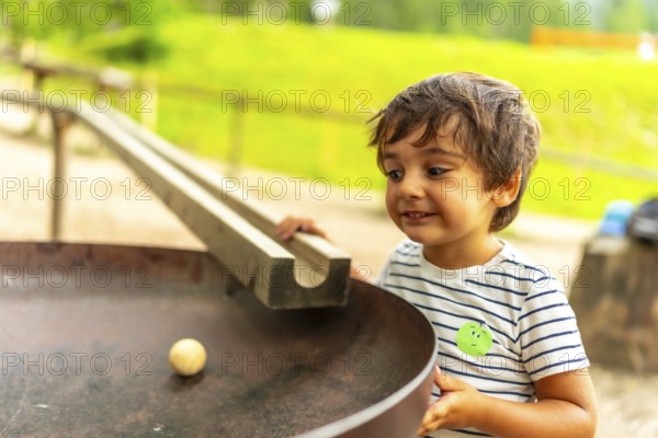 Curious child having fun with a wooden ball rolling down a track in a playground, learning about