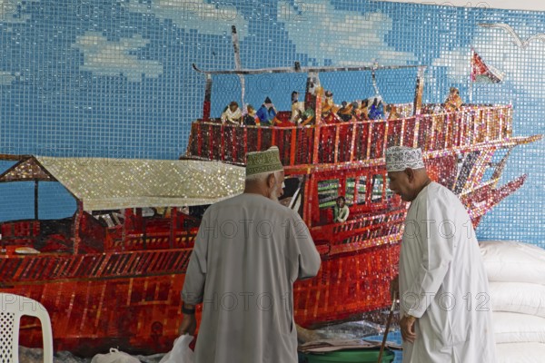 Omani men in dishdashas in front of the wall mosaic of a ship in Muttrah Fish Market, Muscat, Oman,