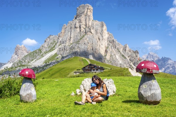 Mother and child relaxing near wooden mushrooms, enjoying breathtaking view of giau pass and