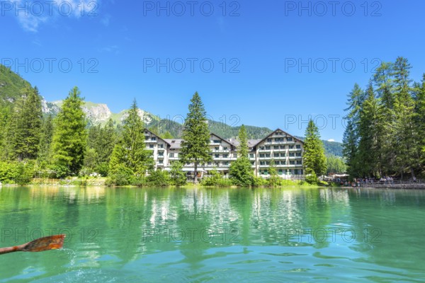 Wooden oar stroking emerald green water of lake braies, with hotel pragser wildsee and dolomites