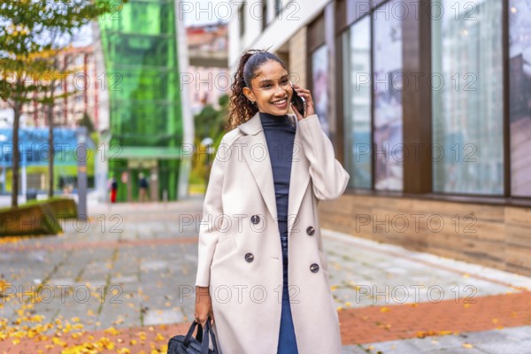 African businesswoman walking while talking to the mobile phone along a city street with fallen