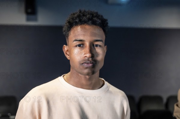 Portrait of a young man standing in a movie theater during a movie session, possibly participating