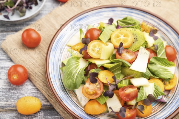 Vegetarian salad of pac choi cabbage, kiwi, tomatoes, kumquat, microgreen sprouts on gray wooden