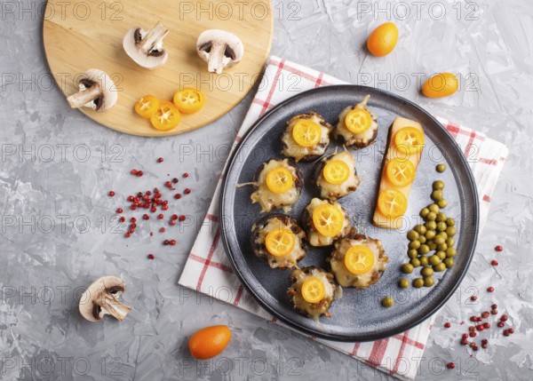 Stuffed fried champignons with cheese, kumquats and green peas on a gray concrete background.
