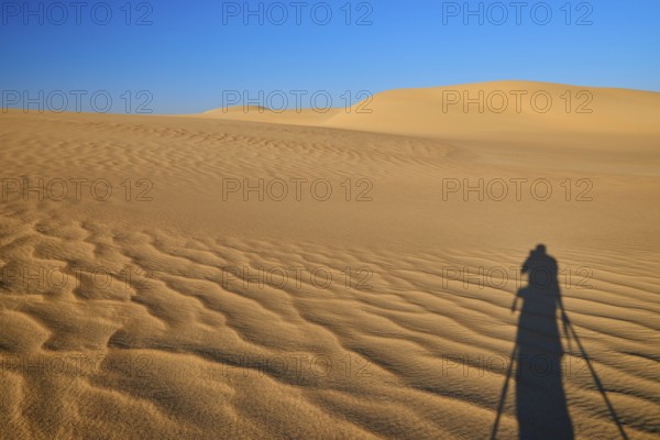 Shadow of a photographer in a vast desert landscape with sand dunes and blue sky, Matruh, Great