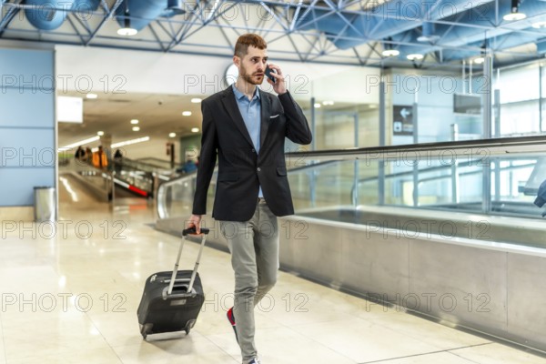 Businessman pulling a suitcase while talking on the phone, confidently walking through a bustling