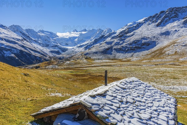 Alpine hut with snow-covered roof, slightly snow-covered alpine meadow, behind the Moiry glacier,