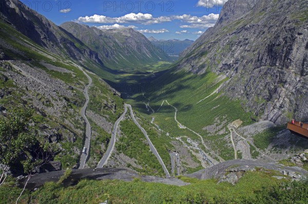 View over a winding mountain road and a narrow valley, rough rocks, small viewing platform,