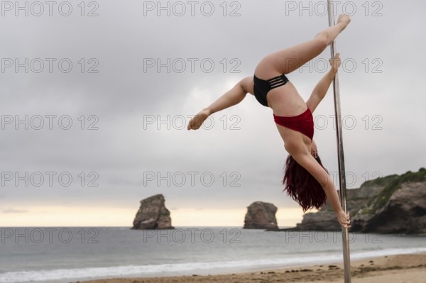 Young caucasian girl doing pole dance at sunrise at a beautiful beach. Acrobatics of pole dance
