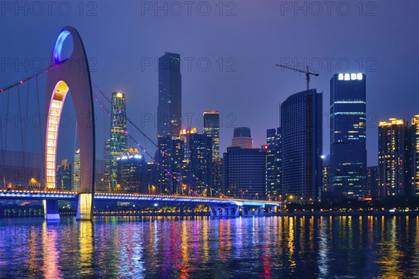 Guangzhou cityscape skyline over the Pearl River with Liede Bridge illuminated in the evening.