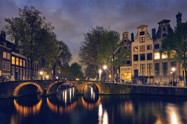 Night view of Amterdam cityscape with canal, bridge and medieval houses in the evening twilight