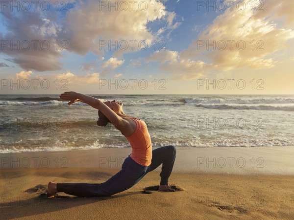 Yoga outdoors, sporty fit woman practices yoga Anjaneyasana, low crescent lunge pose outdoors at