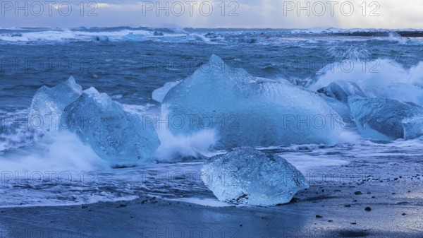Waves breaking on icebergs on the black beach of Breidamerkursandur, near Jökullsarlon, Sudurland,