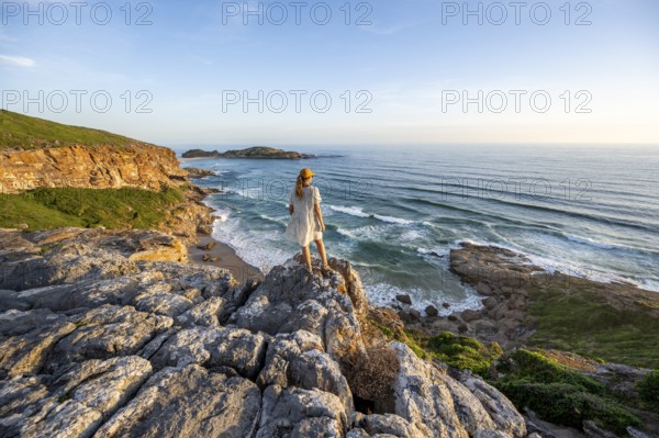 Young woman standing on a rock above the sea in the evening light, beach at The Gap, Robberg