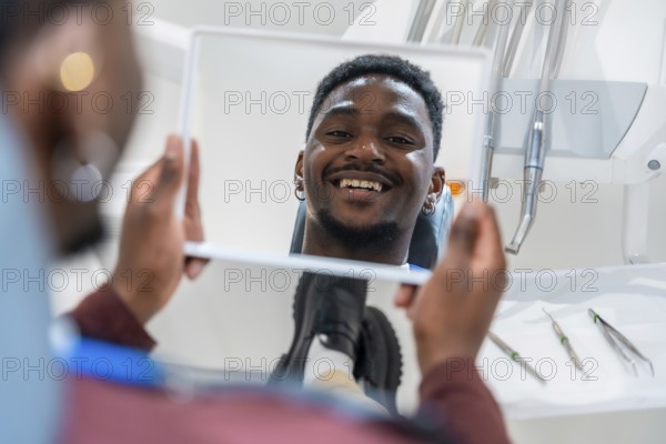 Happy patient looking at his whiter teeth in the mirror at the dental clinic after a whitening