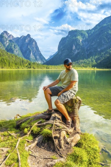 Tourist enjoying the scenic view of lake dobbiaco and the dolomites mountains while sitting on a
