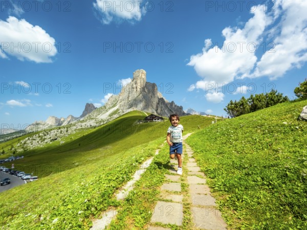 Happy child running on a path at giau pass in the italian dolomites with a mountain peak and blue