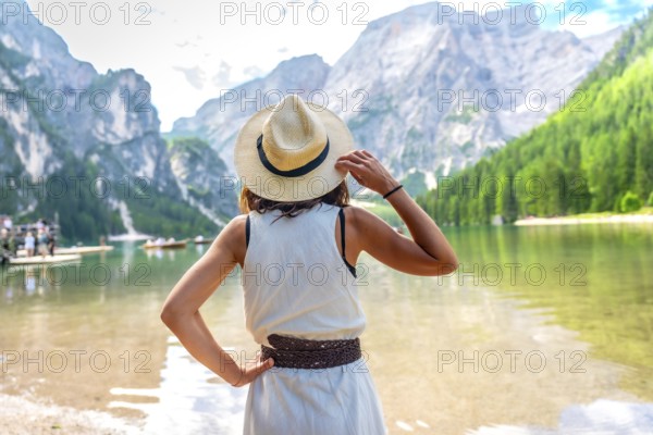 Woman wearing straw hat, enjoying the amazing view of lake braies in the dolomites mountains during