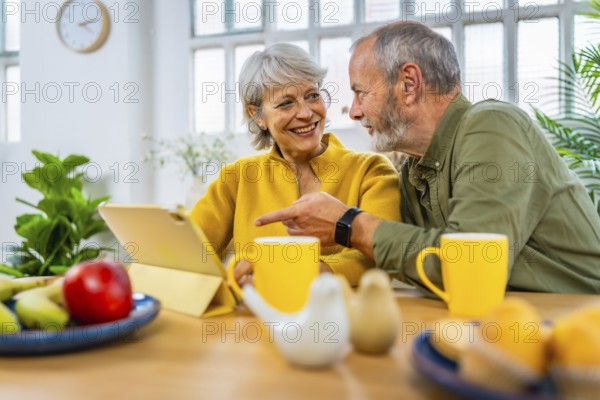 Mature couple exploring the net using digital tablet together at home while having breakfast