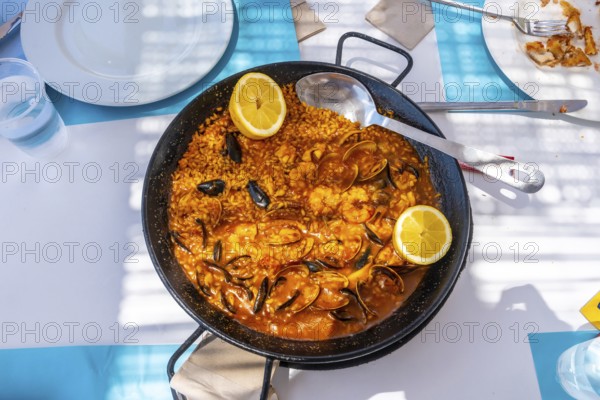 Steaming seafood paella featuring mussels, shrimps, clams, and lemon wedges served in a traditional