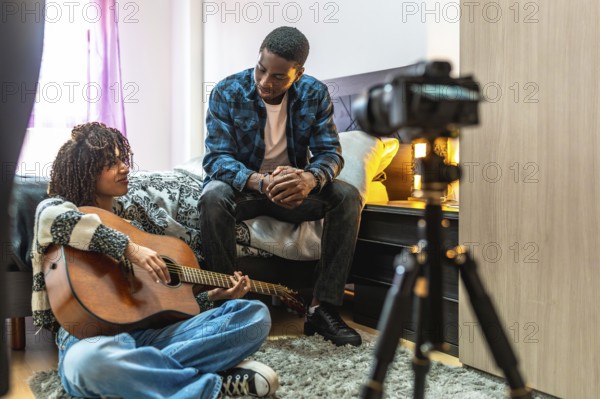 Young woman playing acoustic guitar at home with a friend composing a song and recording a video