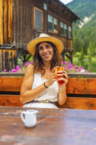 Woman wearing a straw hat enjoying a hot beverage in a mountain chalet by the lake in the italian