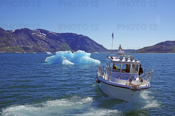 Boat sailing on a blue sea with iceberg and mountains in the background under a sunny sky, small