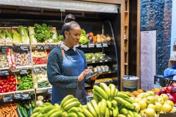 Young saleswoman using digital tablet and managing organic food in supermarket, she's wearing an