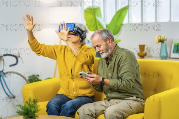 Senior woman using virtual reality googles next to her husband sitting on the sofa using mobile