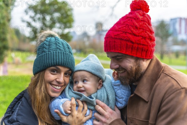 Smiling parents holding their baby, enjoying a joyful winter day together at the park, creating