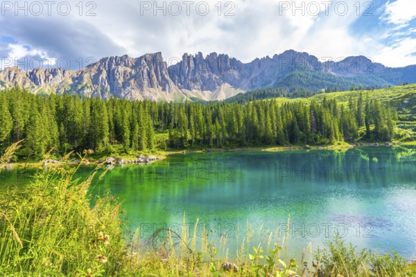 Emerald waters reflecting the latemar group and surrounding pine forest under a blue sky with