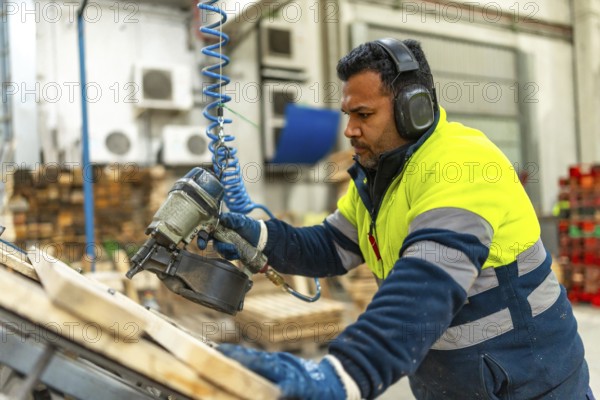 Side view of a caucasian adult man manual worker using compressed air gun to arrange a pallet in a