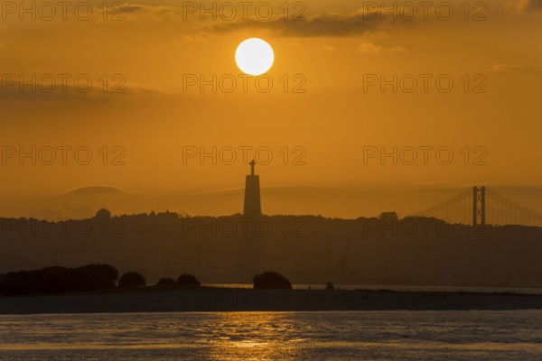 Atmospheric scene with a sunset over a statue and a bridge bathing the water in golden light,