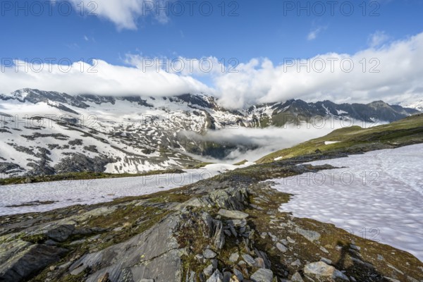Mountain landscape with snowfields and high fog in the valley, behind summit Hoher Weißzint and