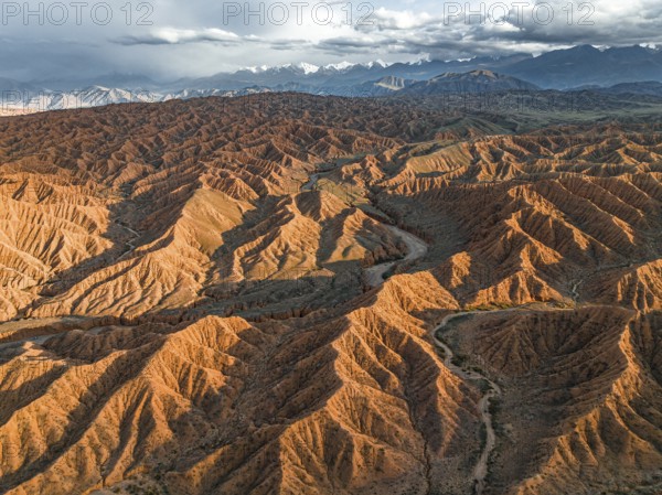 River bed runs through a landscape of eroded hills, badlands at sunset, mountain peaks of the Tian