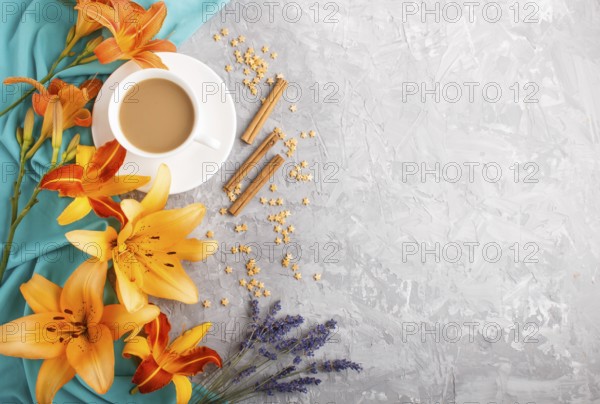 Orange day-lily and lavender flowers and a cup of coffee on a gray concrete background, with blue