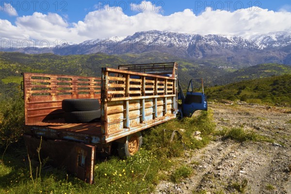 Abandoned rusted lorry in a sunny mountain landscape with snow-capped peaks, wrecked vehicle,