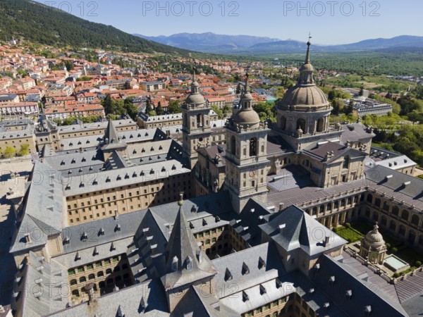 Close-up of a historic monastery with towers, surrounded by a town and mountains in the background,