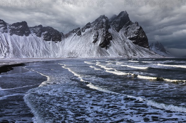 White foamy waves on the beach of Stokkness, behind snowy rocky slopes of Vestrahorn, near Höfn,