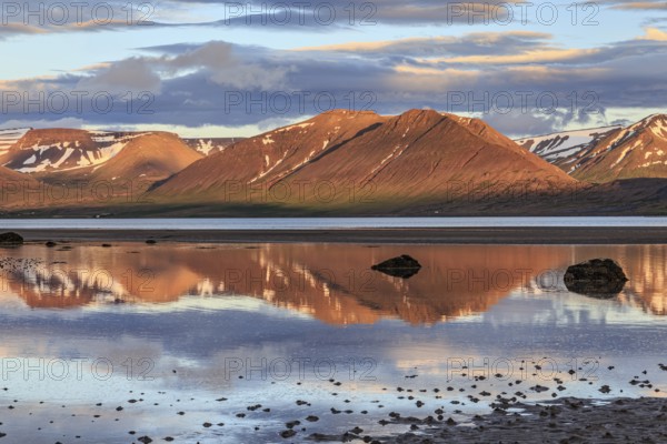 Fjord, low tide, stones, mountains reflected in the water, evening light, cloudy mood, Thingeyri,