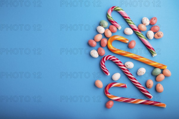 Colorful multicolored candies on a blue background. Christmas cane, chocolate eggs, caramel dragees