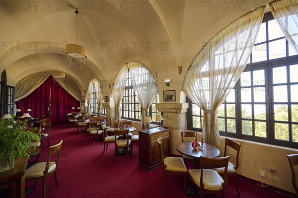 Elegant interior of a restaurant with red carpets, curtains, arched windows and table groups,