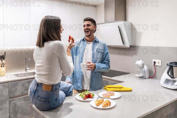 Young couple sharing a lighthearted breakfast in their contemporary kitchen, enjoying strawberries,