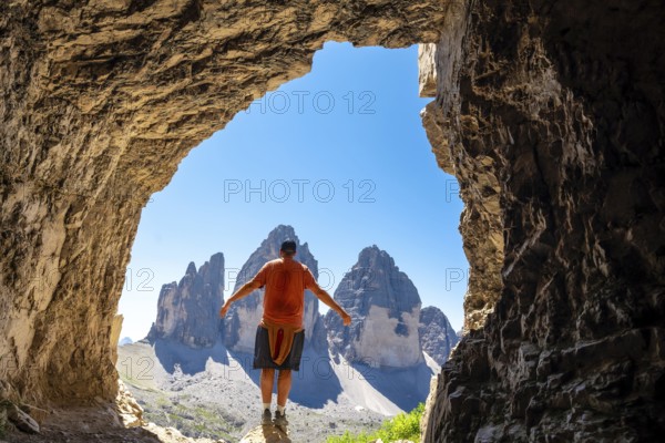 Hiker enjoying the breathtaking view of the tre cime di lavaredo from inside a Tre Cime Cave in the