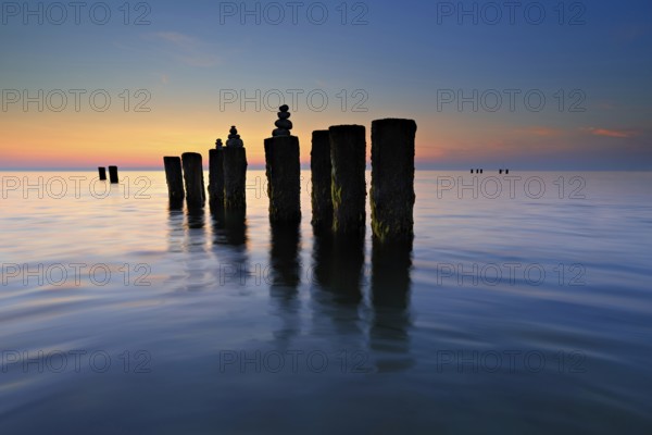 Stone pyramids on old groynes with algae in the water on the Baltic Sea beach at sunset, Wustrow,