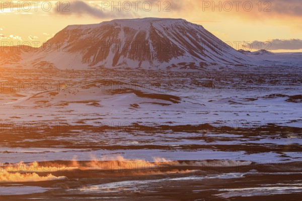 Hot springs and geothermal area in front of mountain landscape in winter, sunbeams, cloudy mood,