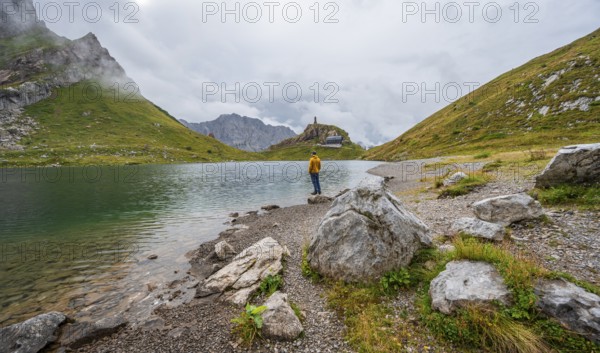 Mountaineer in yellow jacket at the mountain lake, view over the Wolayersee lake to the alpine club