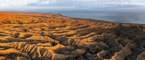 Landscape of eroded hills, badlands at sunset, Lake Issyk Kul in the background, aerial view,