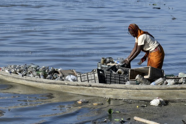 A women rag picker collecting plastic bottle and other plastic materials in a boat from the bank of