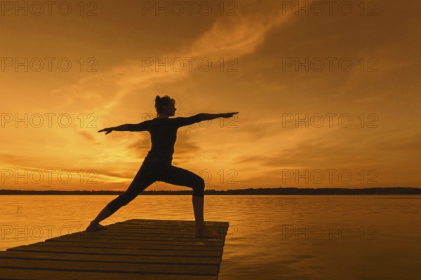 Woman practicing yoga posture Virabhadrasana II, Warrior Pose, lunging standing asana on jetty at